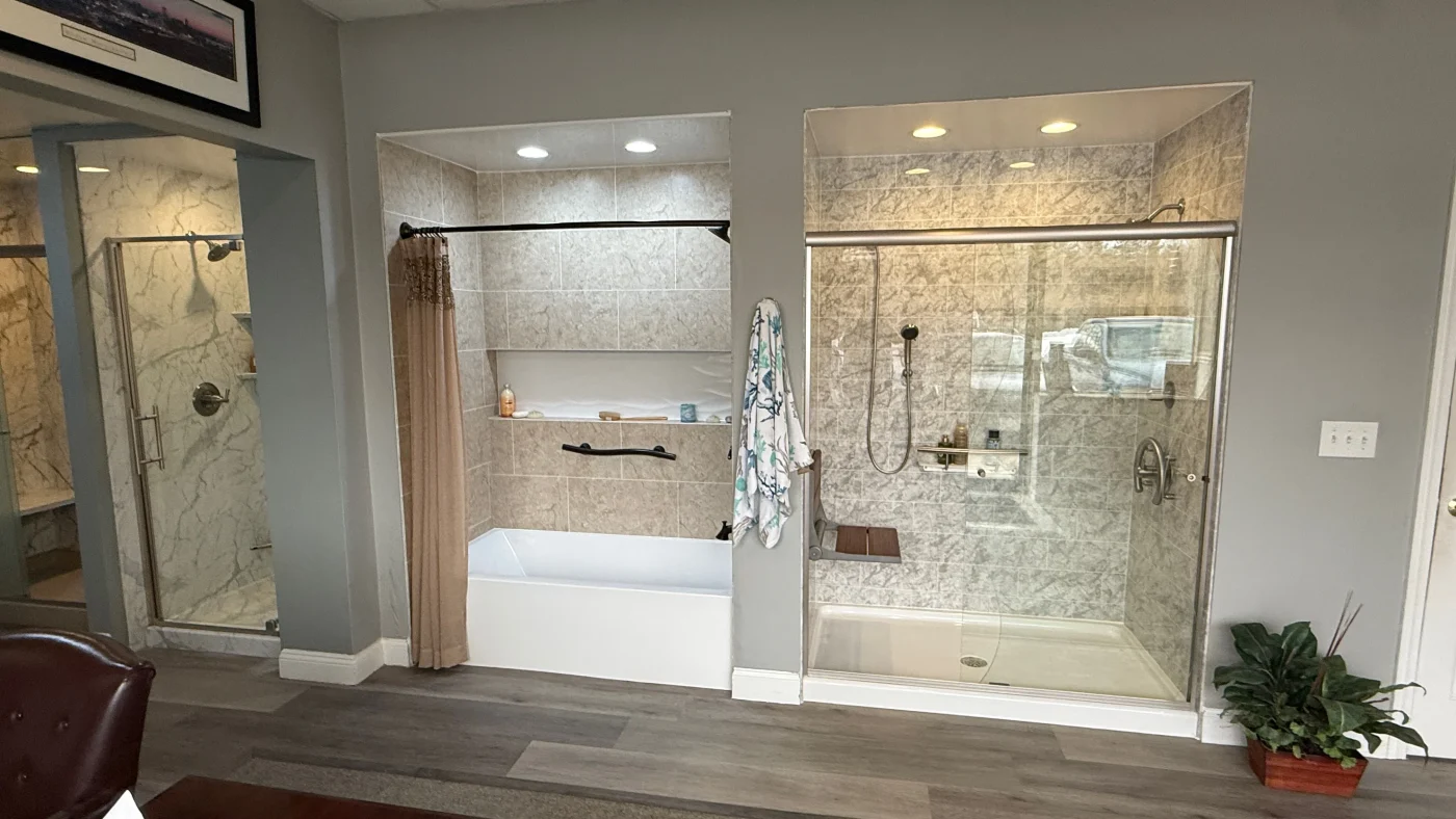A showroom display compares a traditional bathtub alcove with a modern glass walk-in shower designed for a tub-to-shower conversion.